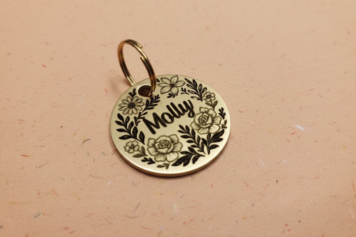 Gold pet tag with floral design and 'Molly' engraved on a wooden surface
