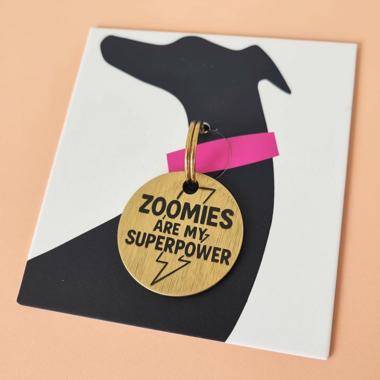 A black dog collar with a gold tag that says "Zoomies are my superpower" in bold text.