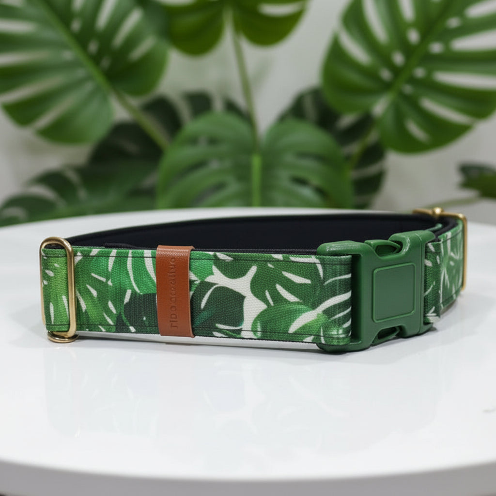 Green leaf-patterned dog collar with gold buckle on a white surface with green leaves in the background