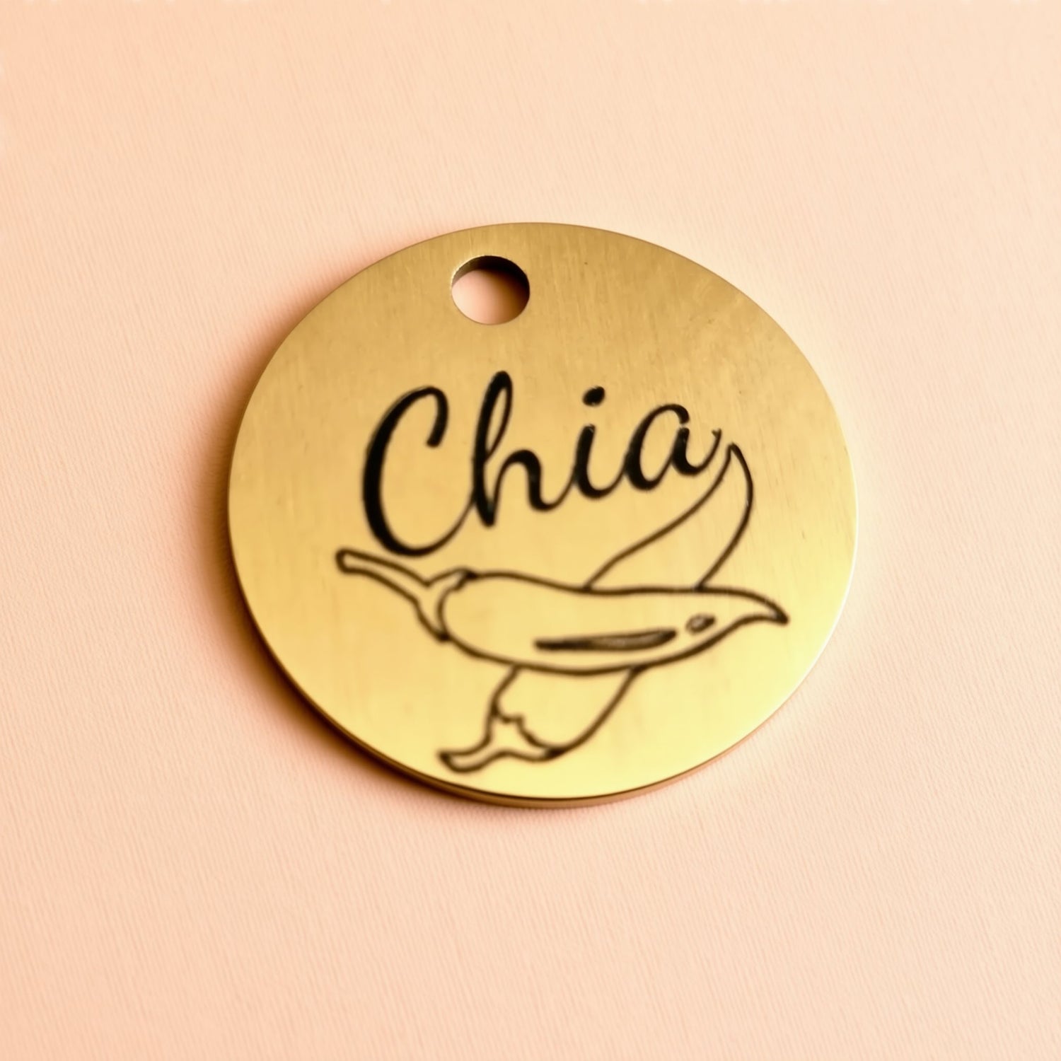 A round metal tag with the word "Chia" printed on it, along with a simple illustration of a pepper.